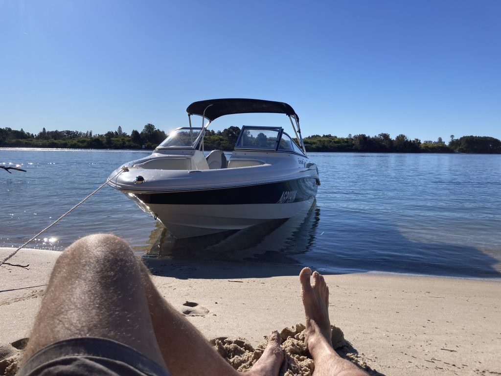 Man Laying down on white sandy beach in Forster next to Speed boat