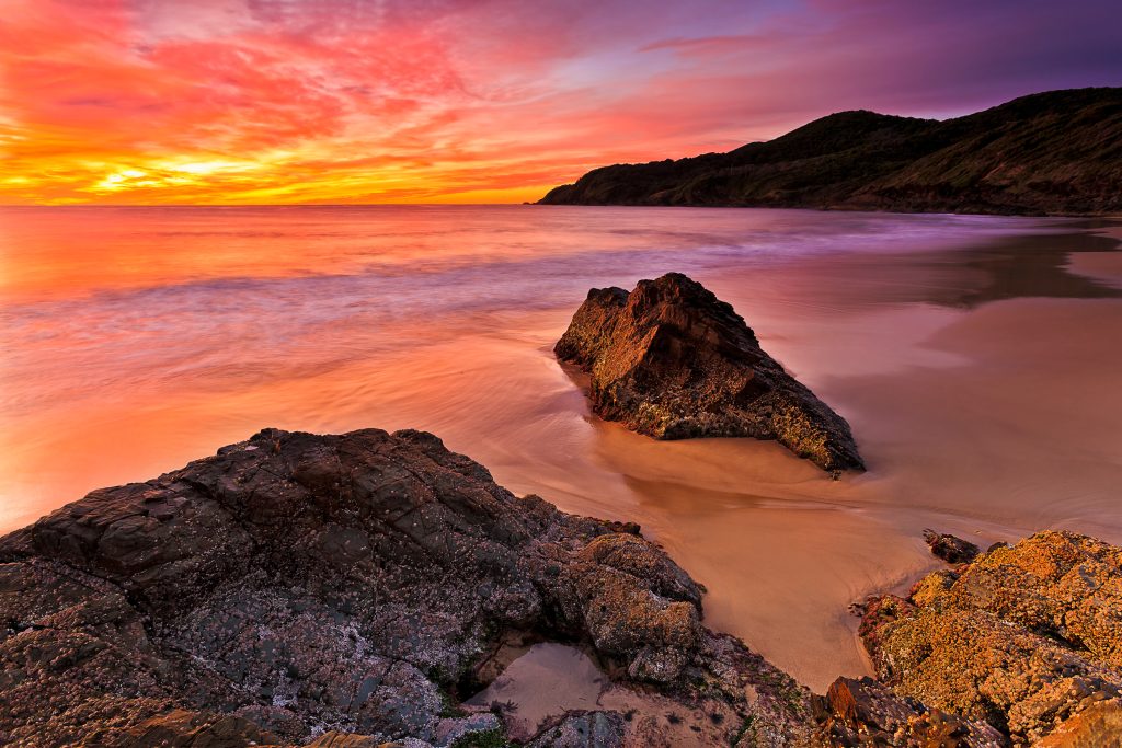 Sunset of Burgess Beach. Bright hot red sunrise over Pacific ocean at Forster town Burgess beach with scenic rock cliffs and smooth sand.